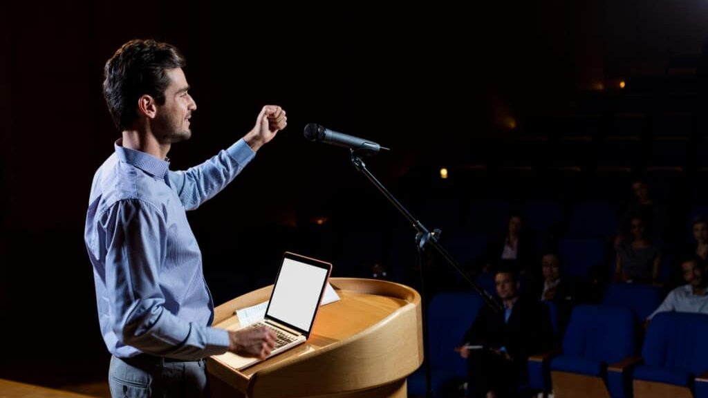 piker təqdimat zamanı auditoriyaya nitq söyləyir, iştirakçılar onu diqqətlə izləyir